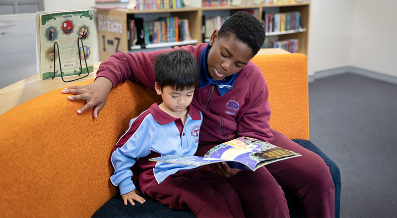 A senior student reading with a kindergarten student in the library at St Bernadette's Primary School Dundas Valley